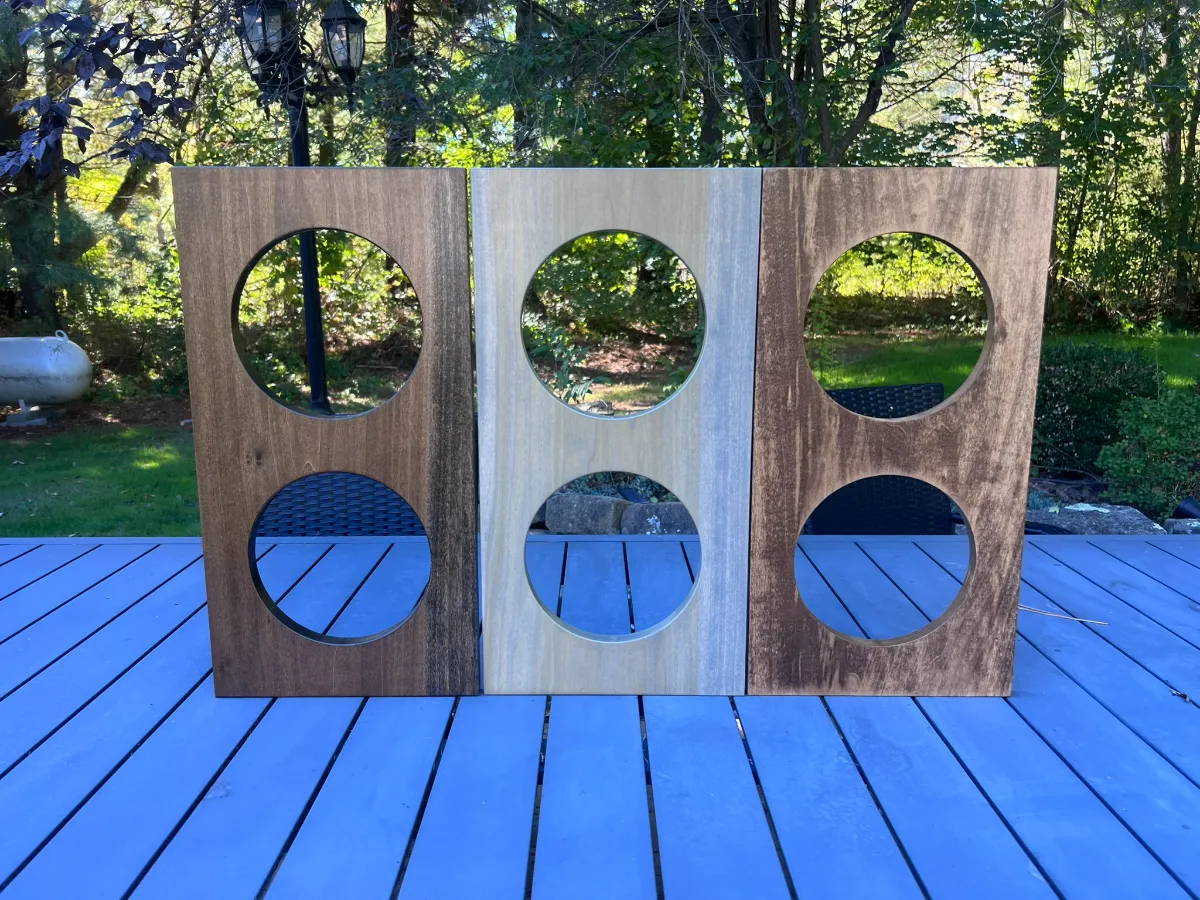 Three poplar stand tops with two round bowl cutouts each, finished in three different stain colors and lined up on a patio table